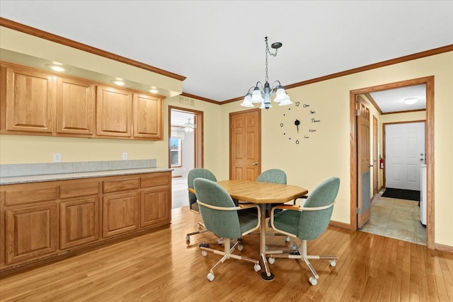 dining space with light wood-style flooring, ornamental molding, baseboards, and a chandelier