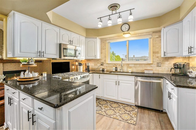 kitchen featuring stainless steel appliances, a sink, dark stone counters, and white cabinets