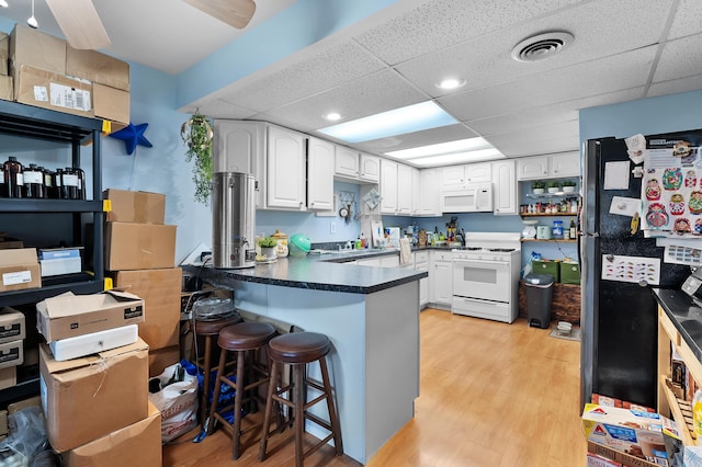 kitchen with white appliances, a peninsula, a paneled ceiling, white cabinets, and dark countertops