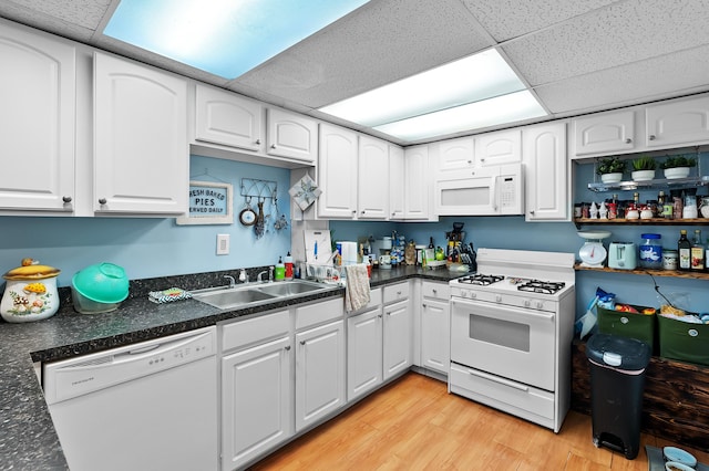 kitchen with white appliances, a sink, light wood-style floors, a paneled ceiling, and dark countertops