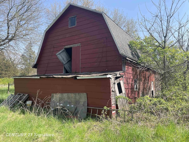 view of property exterior with a barn, a gambrel roof, an outbuilding, and a shingled roof