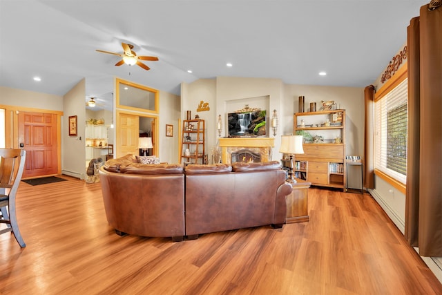 7017 Loud Dr, Oscoda, MI 48750 - living area with ceiling fan, lofted ceiling, light wood finished floors, baseboard heating, and a warm lit fireplace