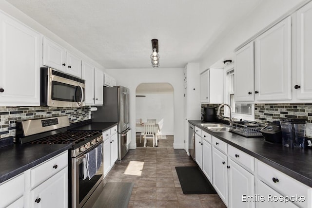 8131 Lorac St, Portage, MI 49002 - kitchen featuring appliances with stainless steel finishes, a sink, arched walkways, dark countertops, and white cabinets