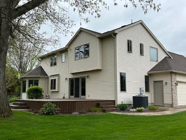 back of house with cooling unit, an attached garage, and a yard