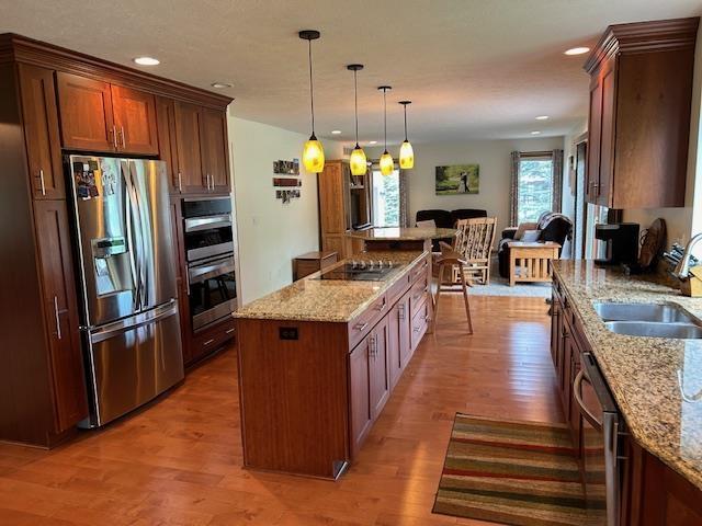 kitchen featuring appliances with stainless steel finishes, a sink, light wood-style floors, a center island, and light stone countertops