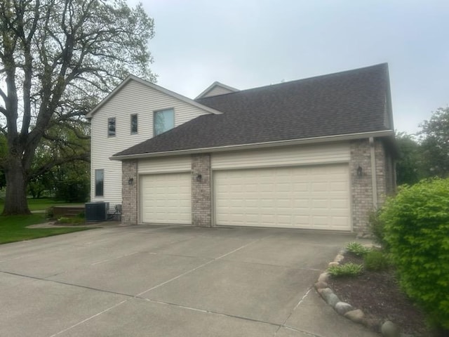 view of side of home featuring brick siding, an attached garage, central air condition unit, driveway, and a shingled roof
