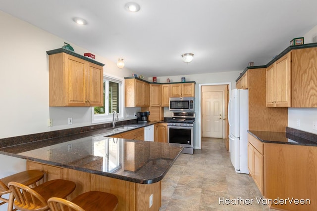 kitchen with stainless steel appliances, a sink, a peninsula, dark stone countertops, and a breakfast bar