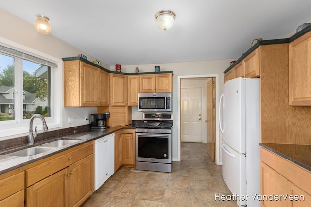 kitchen featuring appliances with stainless steel finishes, a sink, and dark stone counters