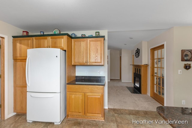 kitchen with freestanding refrigerator, dark countertops, a fireplace with flush hearth, light colored carpet, and baseboards