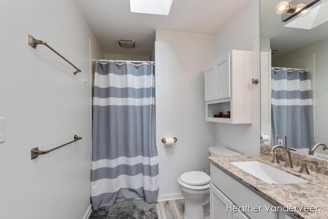 bathroom featuring a skylight, toilet, vanity, wood finished floors, and a shower with curtain