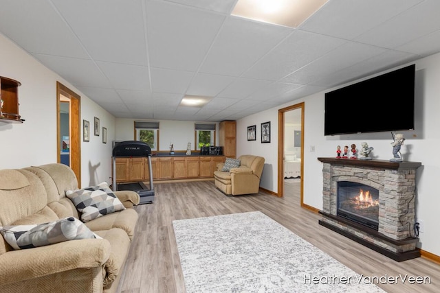 living area featuring a paneled ceiling, a fireplace, light wood-type flooring, and baseboards