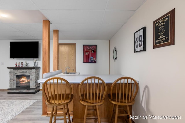 dining space featuring a paneled ceiling, wood finished floors, a stone fireplace, and bar area