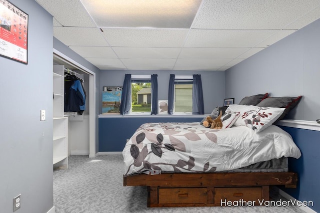 carpeted bedroom with a drop ceiling, baseboards, and a closet