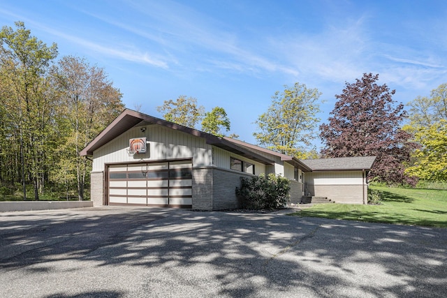 view of front of property featuring brick siding, asphalt driveway, a garage, and a front yard