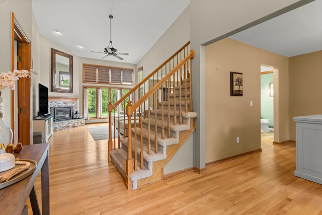 stairs featuring ceiling fan, wood finished floors, a stone fireplace, and baseboards