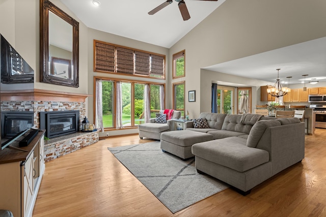 living area with high vaulted ceiling, a ceiling fan, a fireplace, a chandelier, and light wood-style floors