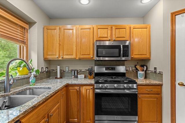 kitchen featuring stainless steel appliances, a sink, tasteful backsplash, light stone countertops, and recessed lighting