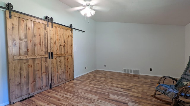 7884 N Saint Helen Rd, Saint Helen, MI 48656 - unfurnished bedroom with a barn door, wood finished floors, baseboards, and a ceiling fan