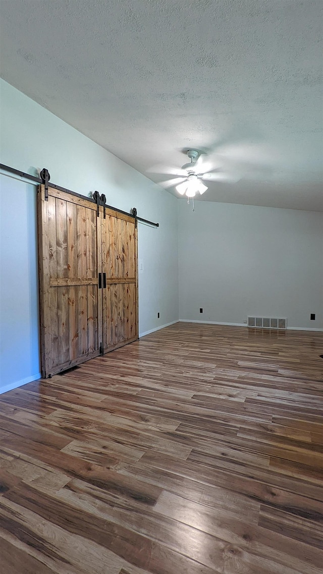 7884 N Saint Helen Rd, Saint Helen, MI 48656 - unfurnished bedroom with a barn door, dark wood finished floors, a textured ceiling, baseboards, and a ceiling fan