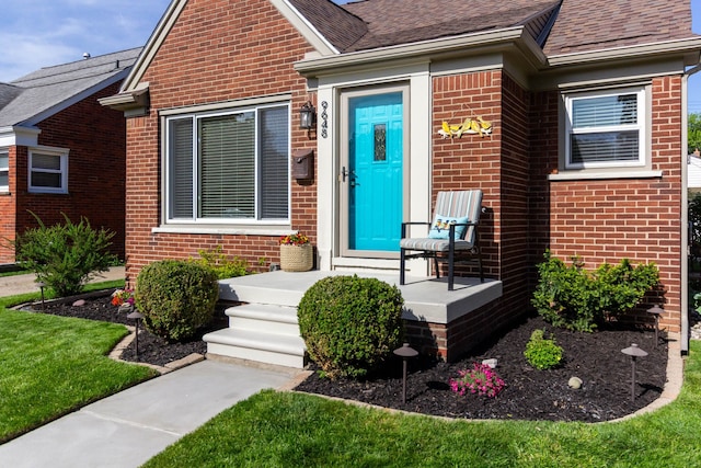 doorway to property featuring brick siding and roof with shingles