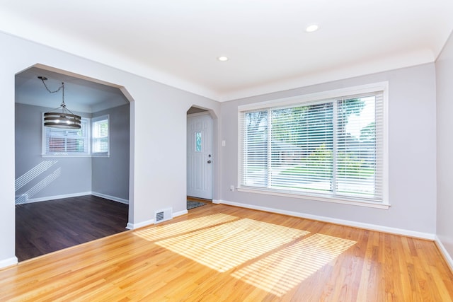 empty room featuring baseboards, wood finished floors, arched walkways, and recessed lighting