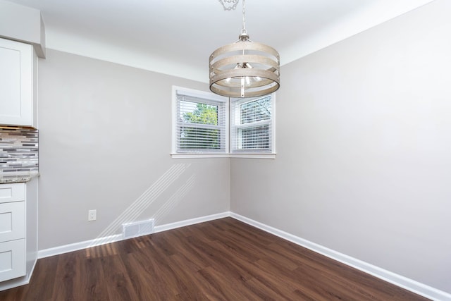 unfurnished dining area with baseboards, dark wood-style flooring, and a chandelier