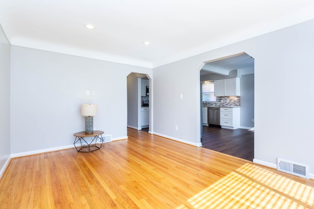unfurnished room featuring arched walkways, wood finished floors, baseboards, and recessed lighting