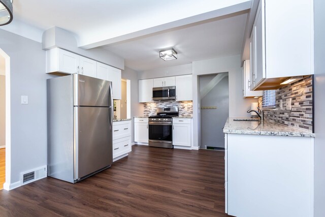 kitchen with appliances with stainless steel finishes, tasteful backsplash, dark wood-type flooring, light stone counters, and white cabinetry