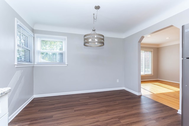 spare room featuring healthy amount of natural light, arched walkways, dark wood finished floors, baseboards, and recessed lighting
