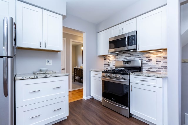 kitchen with appliances with stainless steel finishes, dark wood finished floors, backsplash, white cabinetry, and light stone counters