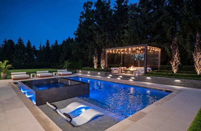 pool at night with an in-ground hot tub, a fire pit, a patio, an outdoor pool, and a pergola