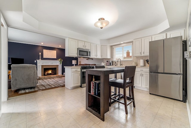 33466 Brownlea Dr, Sterling Heights, MI 48312 - kitchen with appliances with stainless steel finishes, a sink, white cabinets, a brick fireplace, and a breakfast bar area