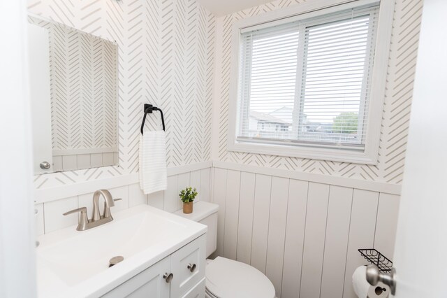 11748 Cloverview Dr, Ravenna, MI 49451 - bathroom with toilet, wallpapered walls, vanity, a decorative wall, and a wainscoted wall