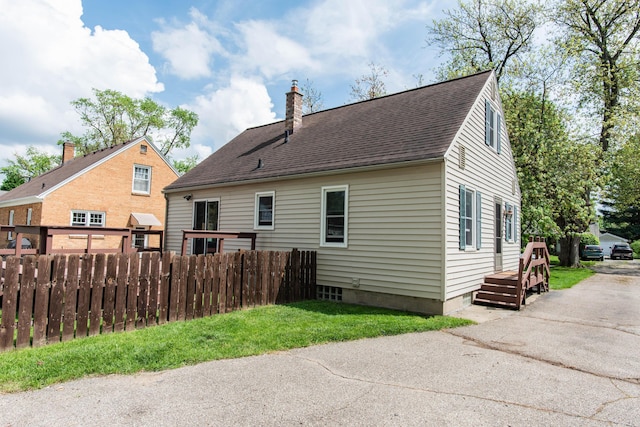 back of house featuring fence, a chimney, and a shingled roof