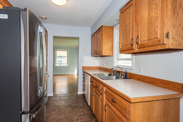 kitchen featuring freestanding refrigerator, a sink, brown cabinetry, baseboards, and backsplash