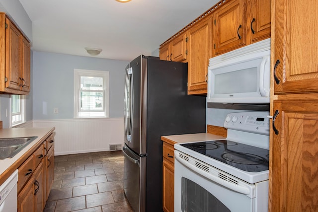 kitchen featuring white appliances, wainscoting, brown cabinetry, light countertops, and a sink