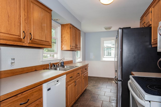 kitchen with white appliances, a sink, brown cabinets, decorative backsplash, and wainscoting