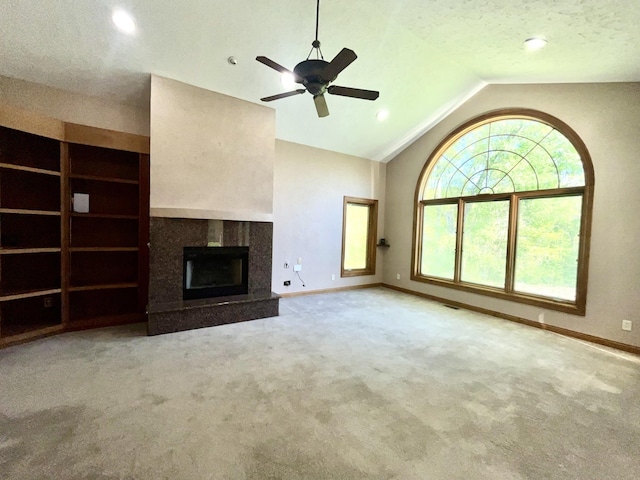 unfurnished living room with baseboards, carpet floors, a tiled fireplace, vaulted ceiling, and ceiling fan