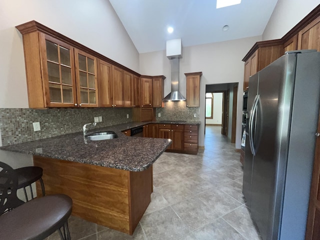kitchen featuring stainless steel fridge with ice dispenser, wall chimney range hood, a sink, a peninsula, and decorative backsplash