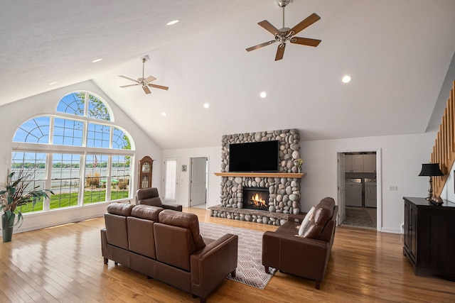 living area featuring ceiling fan, washing machine and clothes dryer, high vaulted ceiling, hardwood / wood-style flooring, and a stone fireplace