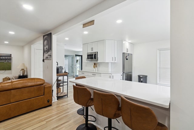 5242 Cedarhurst Dr, West Bloomfield, MI 48322 - kitchen with appliances with stainless steel finishes, light wood-type flooring, white cabinets, light countertops, and a breakfast bar