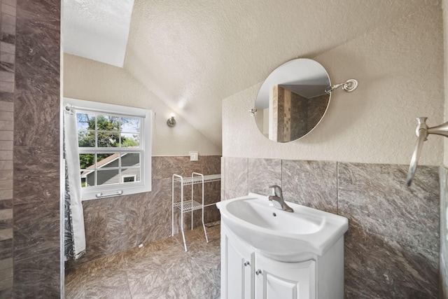 1702 Teneyck St, Jackson, MI 49203 - bathroom featuring tile walls, vanity, lofted ceiling, a textured wall, and wainscoting