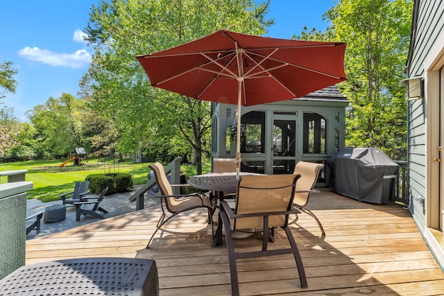 2462 N Dixboro Rd, Ann Arbor, MI 48105 - deck featuring area for grilling, a playground, outdoor dining space, a lawn, and view of scattered trees