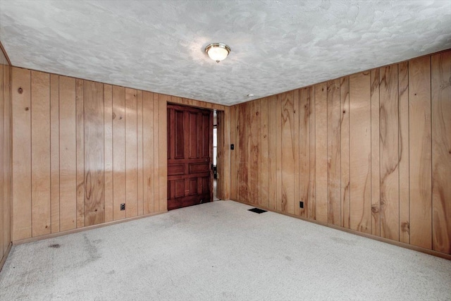 carpeted spare room with wooden walls, a textured ceiling, and baseboards