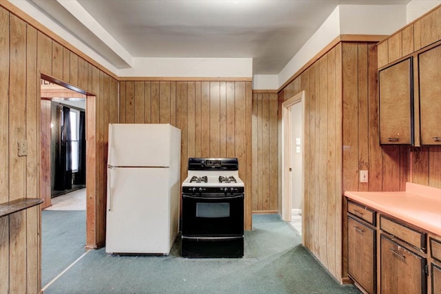 kitchen featuring freestanding refrigerator, range with gas cooktop, carpet, wood walls, and brown cabinetry