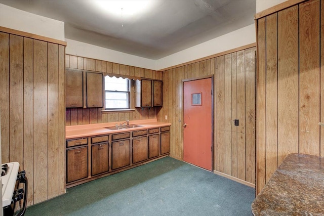 kitchen featuring wood walls, brown cabinetry, range with gas cooktop, dark colored carpet, and a sink
