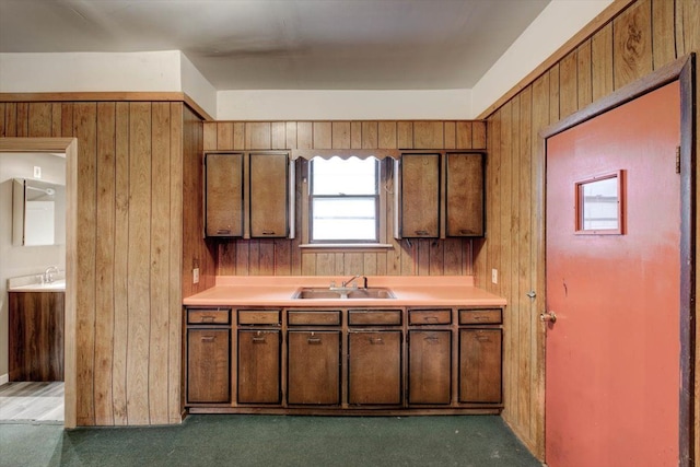 kitchen with a sink, light countertops, wooden walls, and brown cabinetry