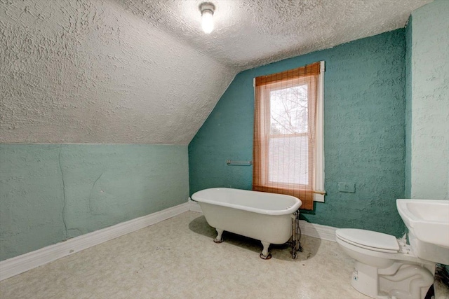 bathroom with a textured ceiling, vaulted ceiling, a freestanding tub, toilet, and baseboards