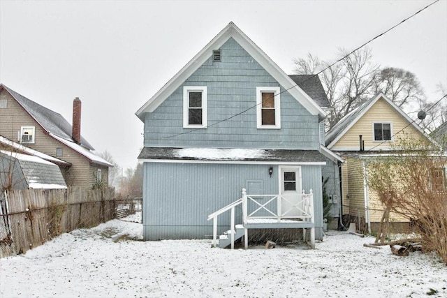 snow covered rear of property with fence and roof with shingles