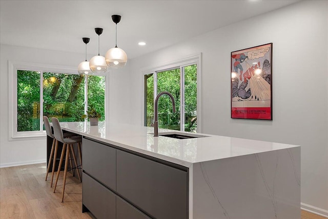7044 Cascade Rd SE, Grand Rapids, MI 49546 - kitchen featuring light wood finished floors, an island with sink, hanging light fixtures, light stone counters, and recessed lighting